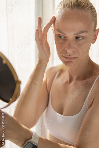 Fotografie Woman scrutinizing her forehead for wrinkles in a mirror, focusing on skin probl