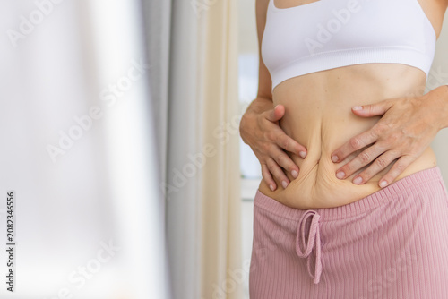 Принти на полотні Woman feeling her sagging stomach skin, reflecting common postpartum body change
