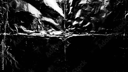 crumpled black metallic foil texture reflects harsh light creating dynamic abstract contrast