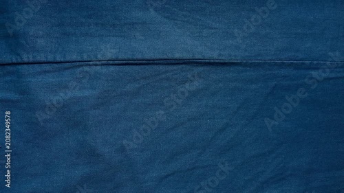 blue denim fabric texture reveals subtle creases along a horizontal stitched seam in a minimalist cinematic overhead view