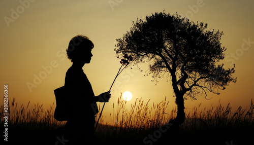 Silhouette of a Child Holding Wildflowers Near a Lone Tree at Golden Sunset