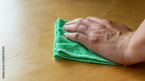 Hand cleaning, in wooden surface, with green cloth, wooden table, with cloth, wood texture, from a close-up perspective, with green, brown accents, and cleaning mood.