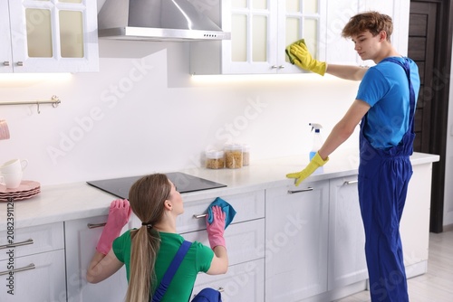Obraz na plátně Teenage workers cleaning cabinets in kitchen. Part-time job