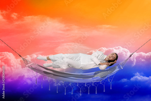 Fotografie Young sleeping woman levitating above hammock against bright sky