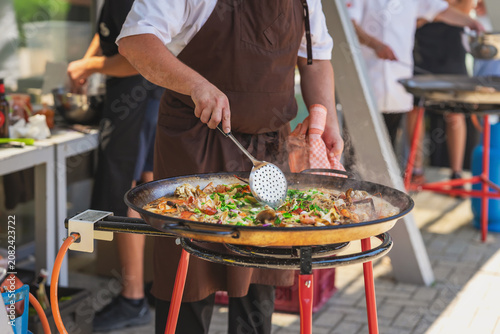 Tableau sur toile Chef cooks paella in pan with seafood, rice, herbs, steam during outdoor catering