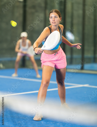 Sportive young woman and other members engaged in Padel Tennis in indoor court of tennis club