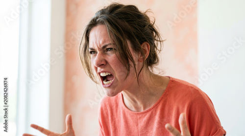 Furious young woman screaming with mouth wide open. Close-up portrait of an angry and frustrated female shouting in rage