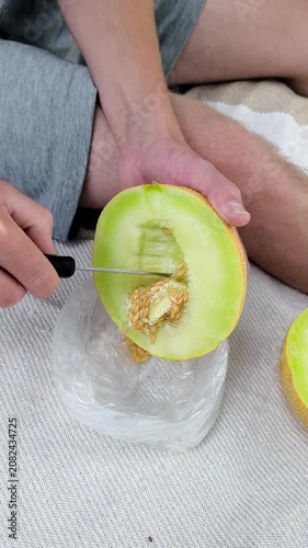 Men's hands removing seeds from a melon. Outdoor picnic.
