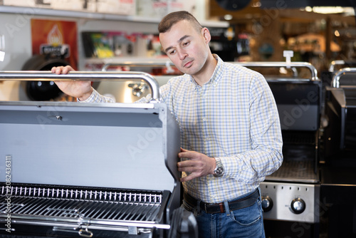 Foto Satisfied customer in a hypermarket chooses a barbecue grill for his backyard