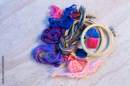Embroidery floss in shades of blue, pink, and purple with wood embroidery hoops on a marbled background.