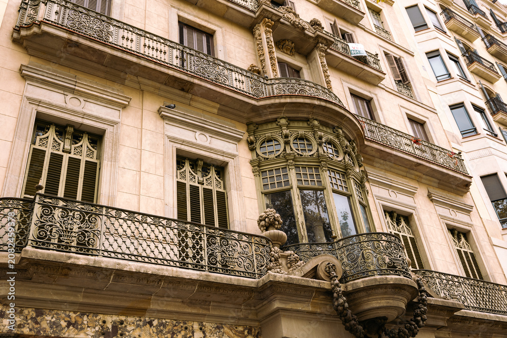 Obraz premium Unique facades of ancient buildings along Passage de Gracia Street, decorated with columns, statues, with carved balcony railings. Details of authentic buildings located on main avenue of Barcelona