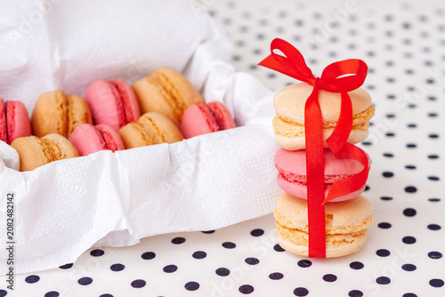 Three pink and beige macarons tied with a vibrant red ribbon beside an open white box filled with French sweets.