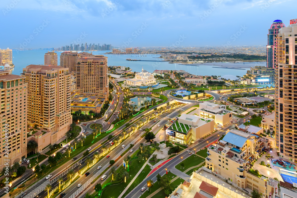 Fototapeta premium Twilight view of the Doha skyline with the Doha Pearl island and Sheikh Hamad bin Jassim Mosque in view along the Persian Gulf in Doha Qatar.