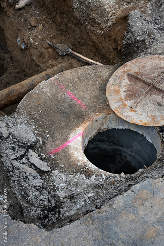 Underground utilities construction project, precast concrete stormwater system access vault in dirt trench under road, old iron pipe, shovel and tamper bar
