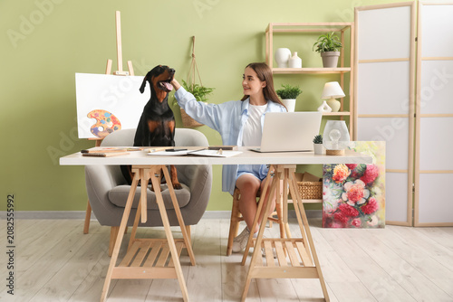Εκτύπωση καμβά Cute Doberman dog and beautiful young happy woman with paints palettes working a
