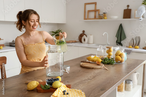 Young woman pouring lemonade into jar in kitchen