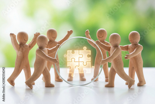 Wooden figures working together around a glowing puzzle symbol