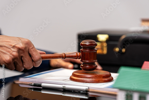 Close-up of a hand holding a wooden gavel over documents on a desk in a legal office, with a briefcase and pen in the background