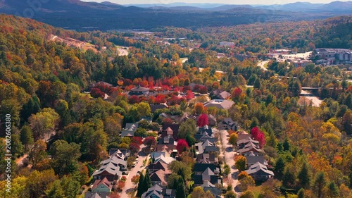 Scenic mountain community with private homes surrounded by dense woodland glowing with vibrant autumn colors. Aerial view of peaceful countryside living.