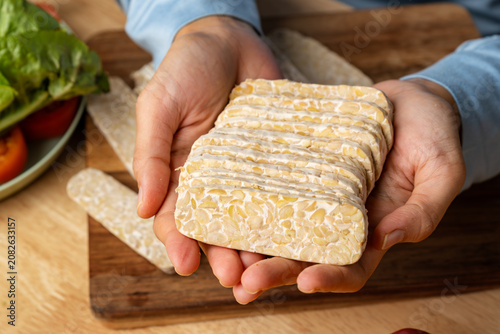 Hands Slicing Fresh Tempeh on a Wooden Cutting Board, Healthy Cooking Concept