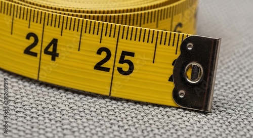 Close-up of a yellow measuring tape showing the numbers 24 and 25 on a gray surface.
