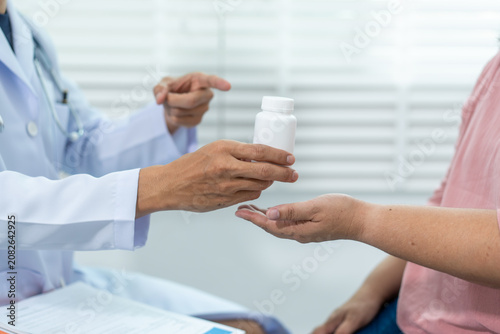 Doctor handing a pill bottle to a patient during a medical visit in a clinic, showing prescription medicine, healthcare advice, and treatment support.