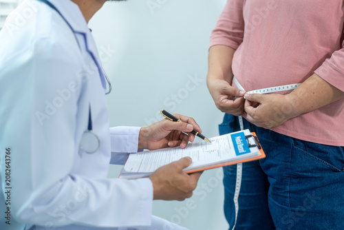 Close-up of a healthcare worker measuring an overweight woman's waist with tape, showing weight control, obesity risk, body size check, and healthy lifestyle support.