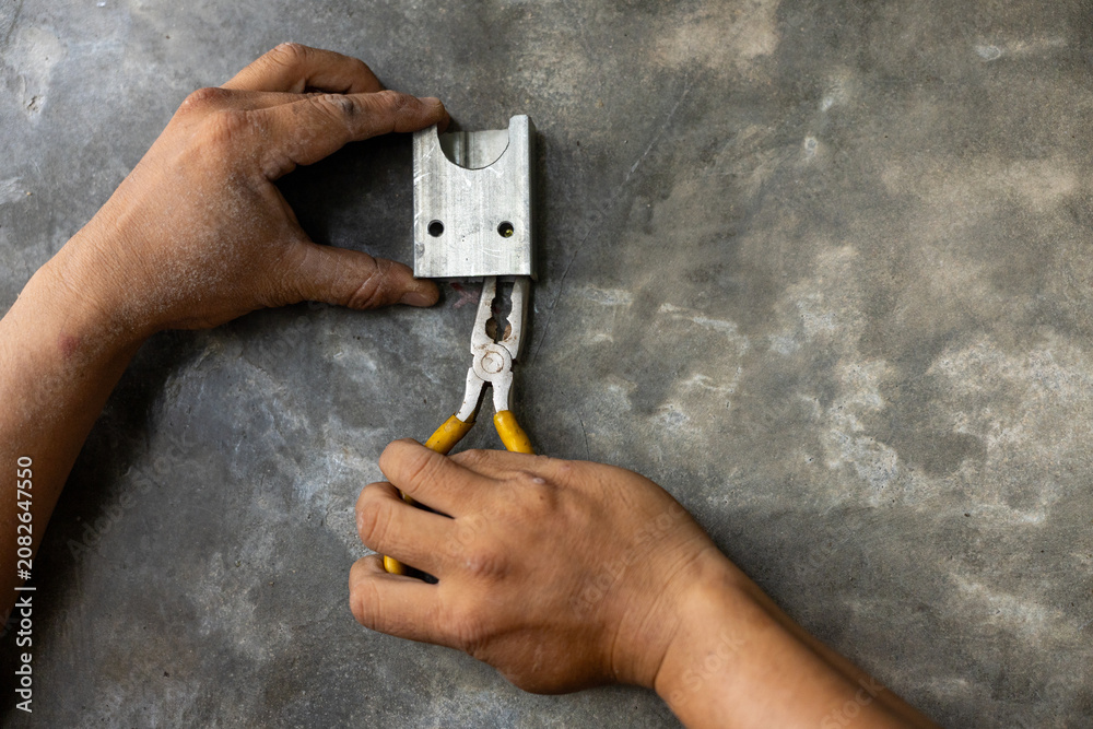 Fototapeta premium Metal lock repair with pliers by worker hands on concrete surface, closeup of manual locksmith work with tool and padlock part, industrial maintenance and fixing concept