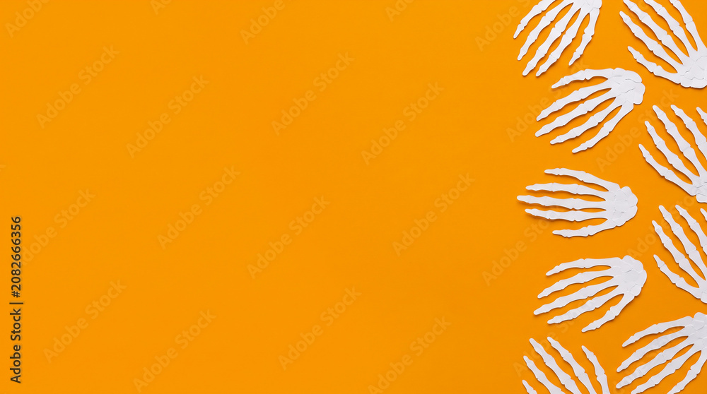 Fototapeta premium Halloween orange background featuring skeleton hand paper cut out right border, copy space for spooky party invitation, greeting card, banner, poster, flyer and creepy autumn holiday design