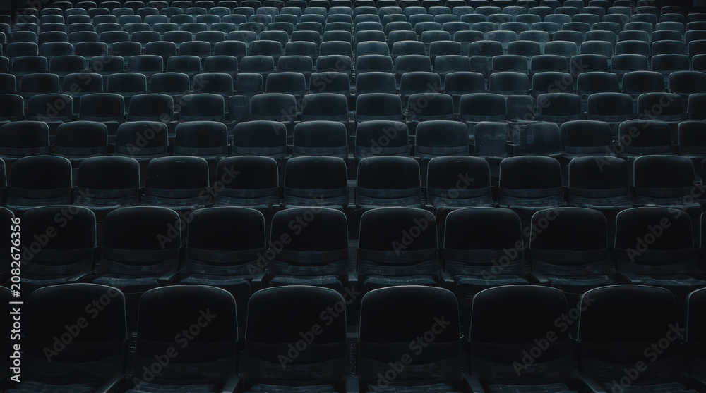 Obraz premium Empty auditorium seats arranged in repeating rows under moody lighting evoking solitude