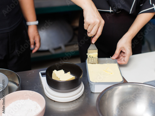 Asian woman preparing ingredients scooping butter into bowl weighing it kitchen digital scale mixing flour cocoa powder sugar make delicious homemade brownies dessert cake recipe baking process bakery