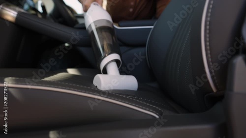 close up hand of woman using portable handheld vacuum cleaner to clean dust on leather car seat of electric car
