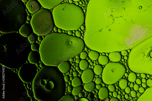 Green oil bubbles floating in liquid create vibrant abstract macro texture with dark contrast