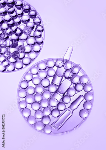 Medical ampoules and gel granules in Petri dish, purple background. Laboratory cosmetology, biotechnology, anti-aging skincare, scientific innovations
