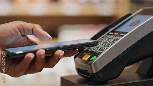 Customer's hand holding a smartphone and making a contactless payment using an nfc banking terminal at a retail store checkout, ensuring a fast and secure transaction