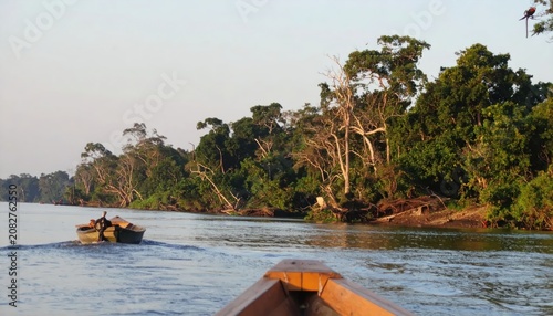 Wooden boat following another vessel on a jungle river.
