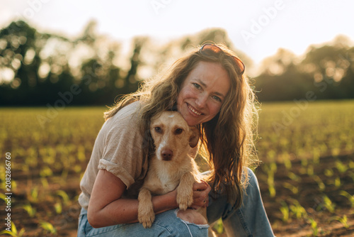 Woman embracing small dog in field at sunset