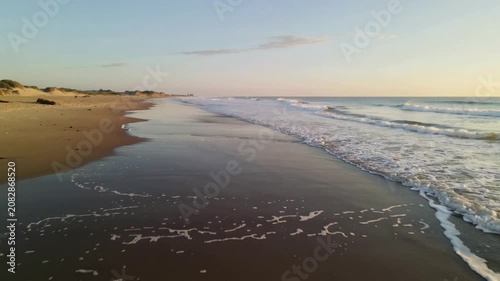 Gentle ocean waves crashing on a sandy beach at sunrise