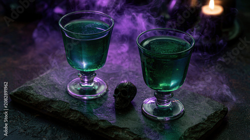 Two glasses with green potion and small skull decor on stone board. Magical drink with purple smoke around. Spooky atmosphere for Halloween party table decoration. Festive eerie concept.