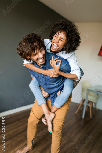 Cheerful man carrying girlfriend piggyback at home
