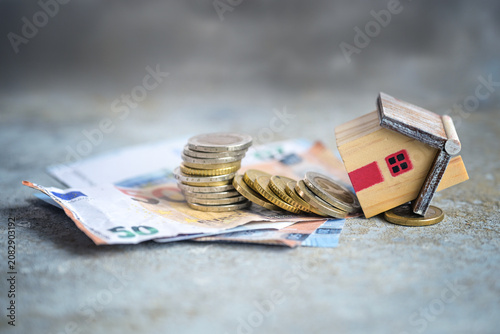 Quadro su tela Financing failed, house model crashed down with a stack of coins and banknotes,
