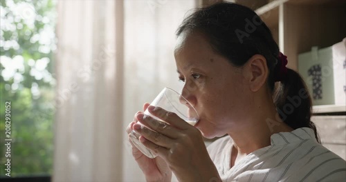 Close up face. Asian Woman Drinking Soy Milk from Glass in Living Room, Female Enjoying Plant-Based Milk Alternative by Window with Morning Sunlight and Curtains, Healthy Lifestyle Routine.