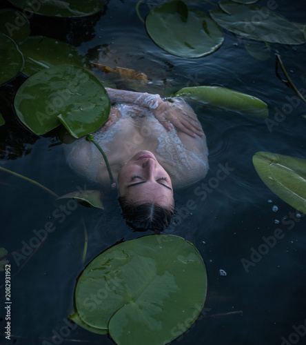 Canvas Print Mystical Slavic mermaid floating in deep lake water among green water lilies, pa