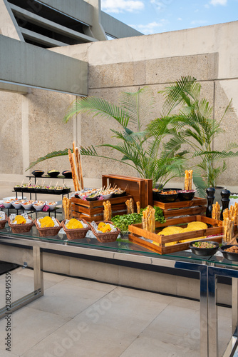 Elegant outdoor catering buffet table featuring a variety of tacos, breadsticks, and appetizers arranged in wooden crates and baskets on a modern terrace setting.