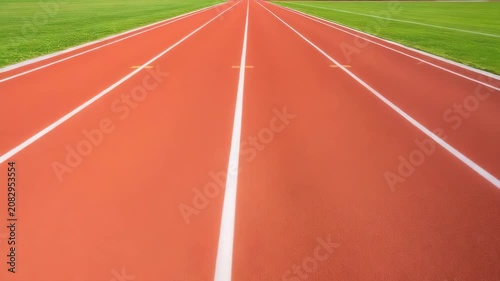 Empty running track with red surface and green grass surroundings,   Cinematic slow drone flight along the running track