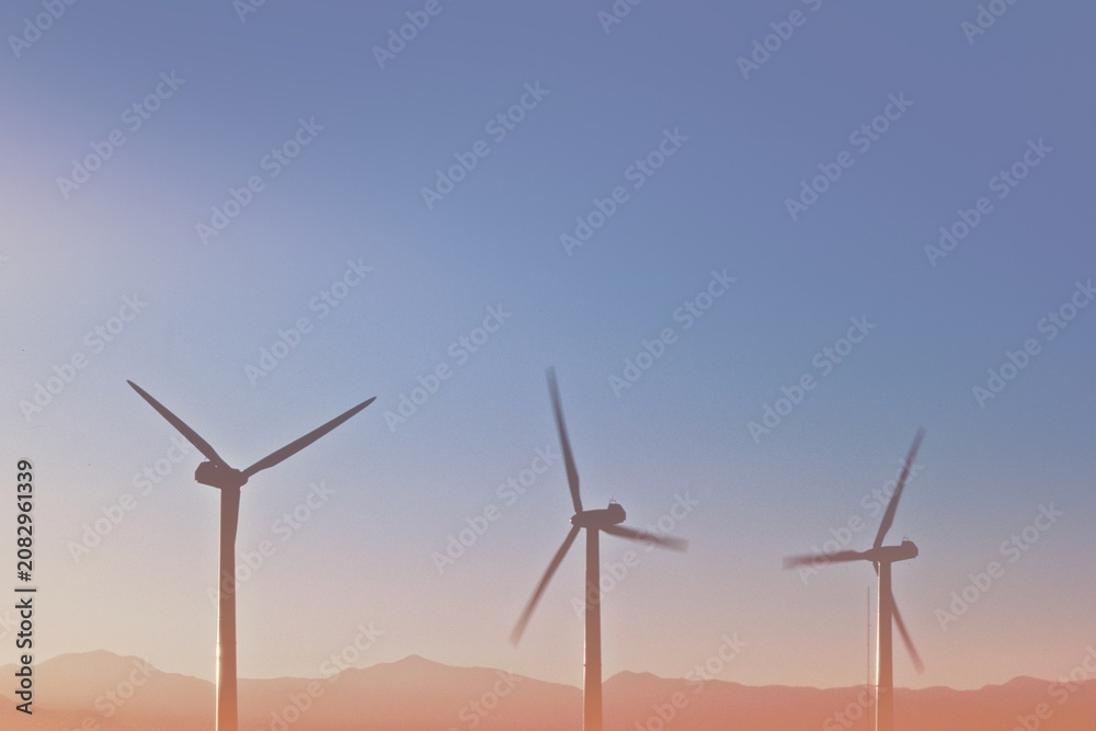 Obraz premium Three wind turbines against a clear sky and distant mountains.
