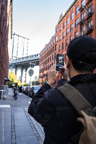 Tourist taking a photo of the Manhattan Bridge in DUMBO, Brooklyn. DUMBO is a popular photography destination in New York City.