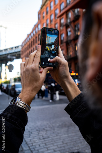 Smartphone capturing the iconic Manhattan Bridge view on Washington Street in DUMBO. DUMBO is a famous tourist destination in Brooklyn.