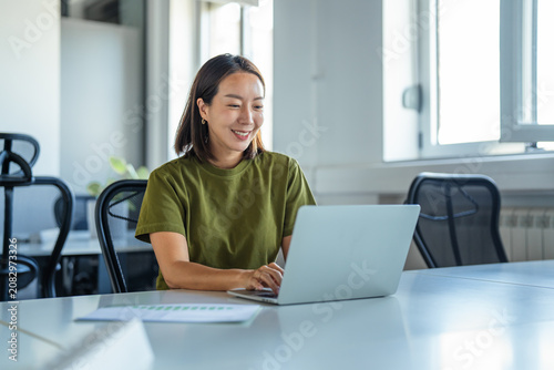 Fotografie Young asian woman smiling while working on laptop