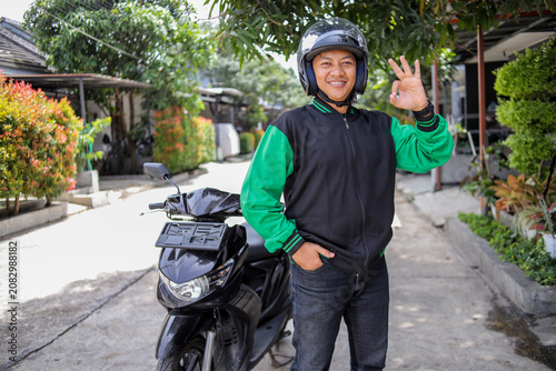 Indonesian Online Motorcycle Taxi Driver Showing an OK hand Sign Next to His Scooter